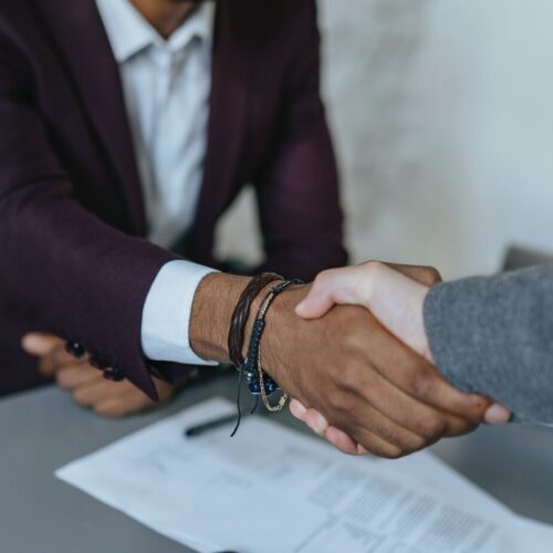 Two people are closing a job interview with a handshake. There is a resume on the table below, and both people are wearing sport jackets and shirts.
