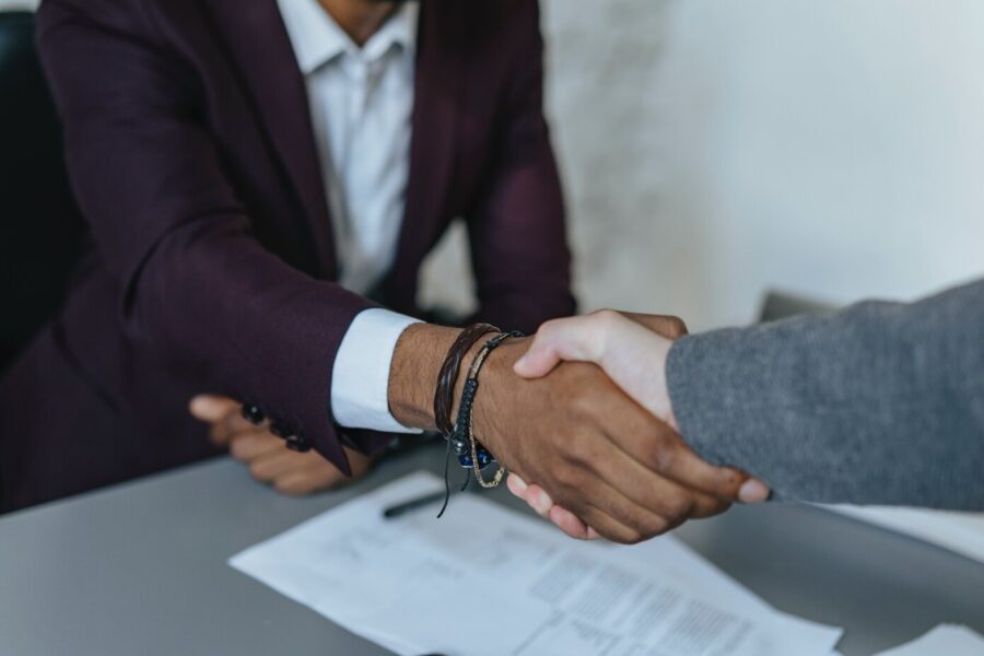 Two people are closing a job interview with a handshake. There is a resume on the table below, and both people are wearing sport jackets and shirts.