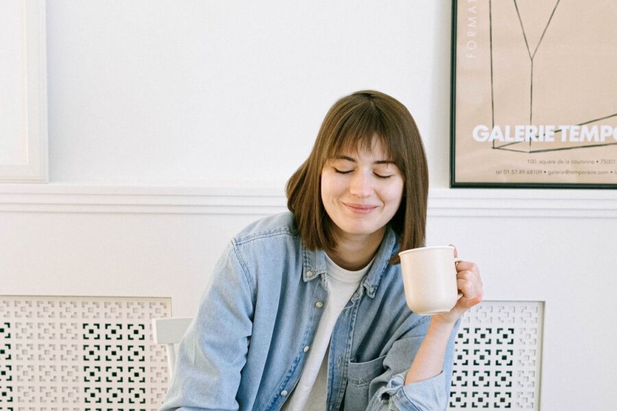 A woman is smiling, looking at a laptop. She is holding a cup of coffee in her hand.