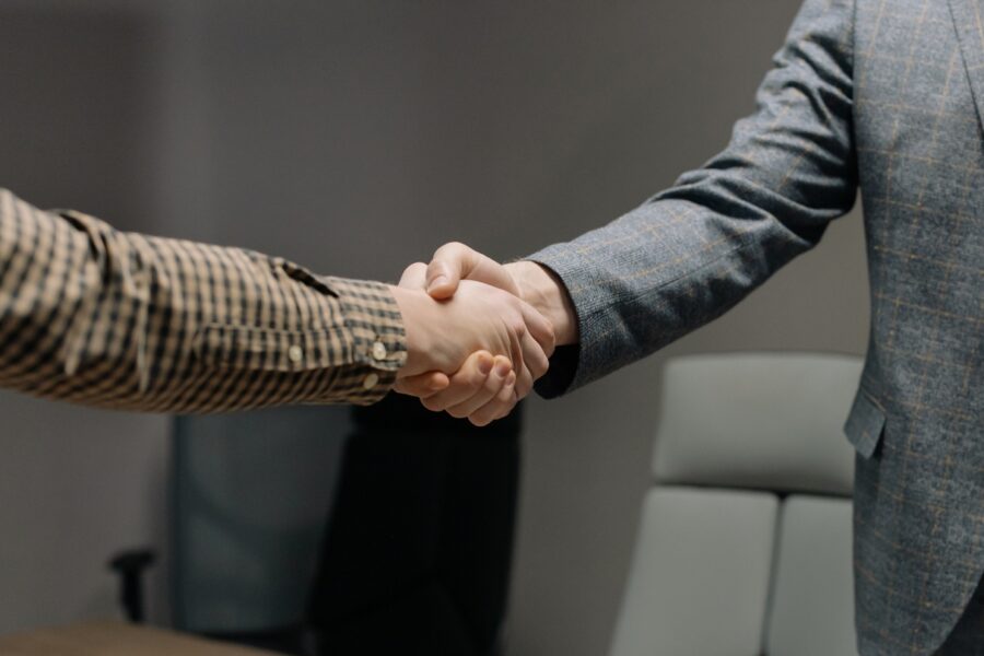 Two men are shaking hands. They are both in business attire.