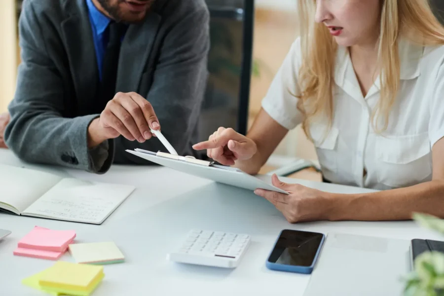 Two colleagues reviewing recruiting costs on a clipboard at a desk with a calculator