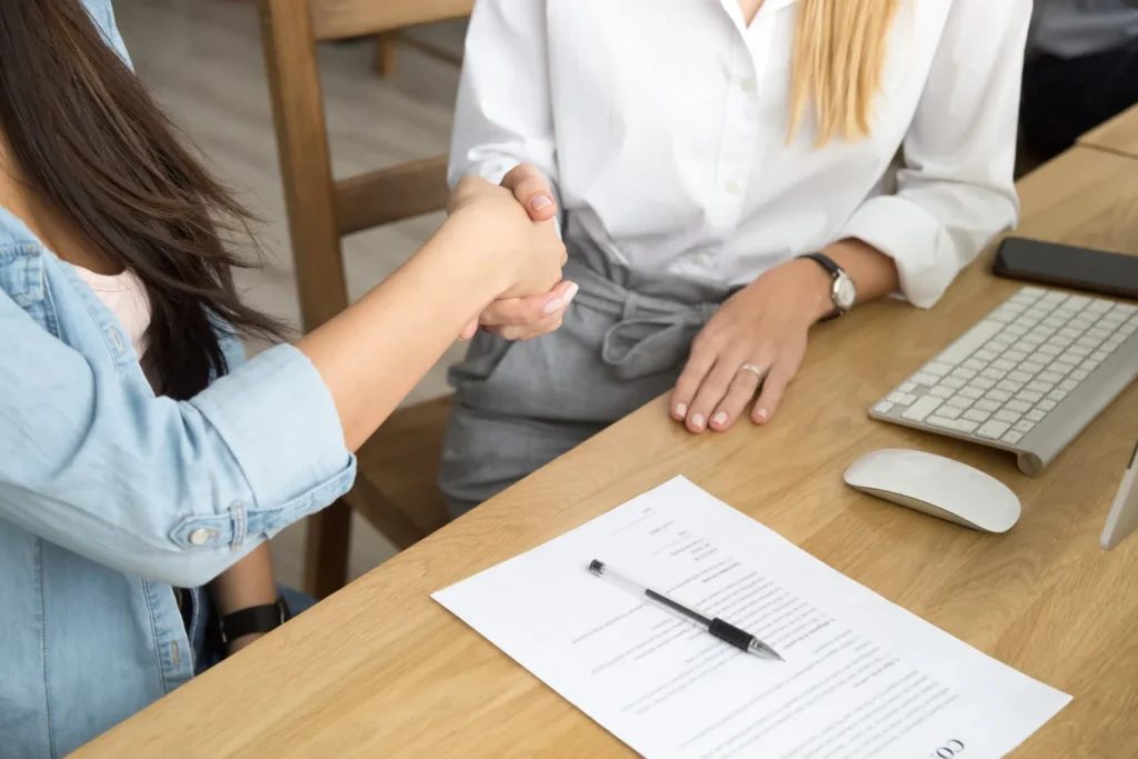Hiring manager shaking hands with a new hire over a signed job offer