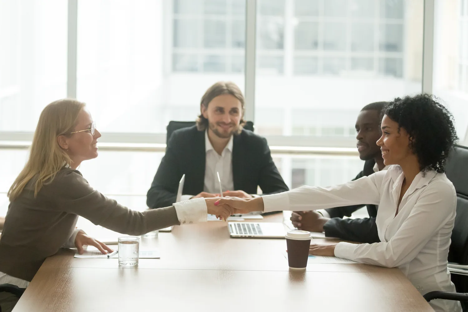 Two professionals shaking hands across a conference table during a business meeting